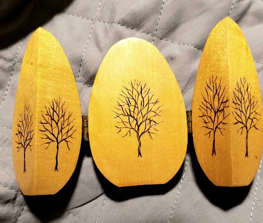 Wood egg opened on its hinges to reveal five leafless trees delicately woodburned into each flat face. 